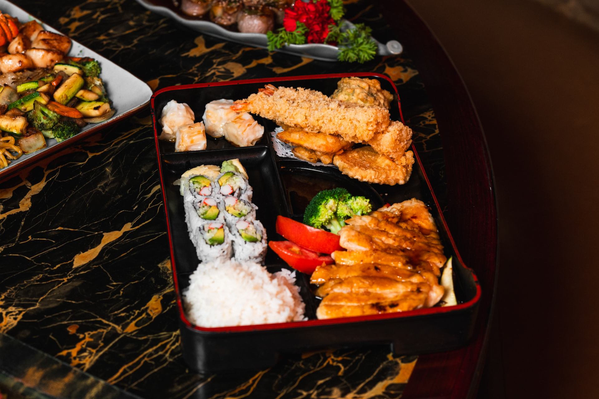 Japanese bento box with tempura, California roll, rice, teriyaki chicken, and vegetables at Kumo 27